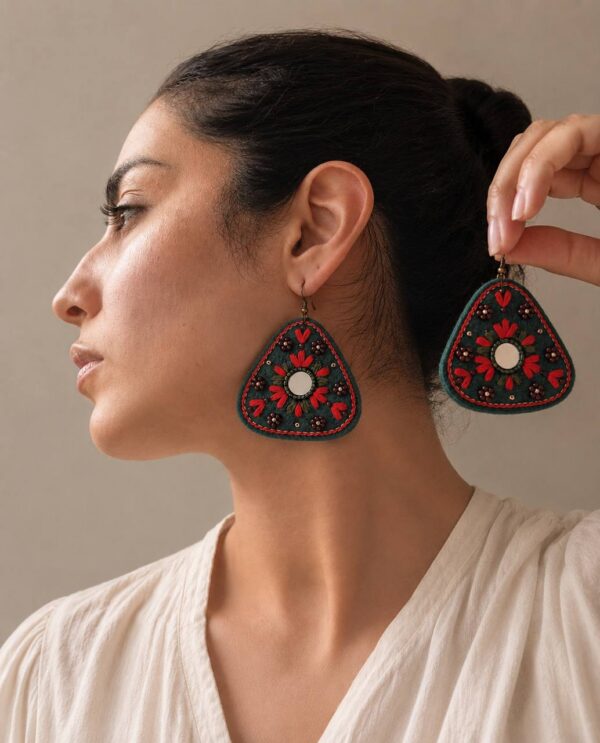 Model wearing dark green and red triangular embroidered earrings with reflective centres