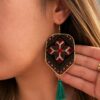 Model wearing floral embroidered shield earrings with green tassels