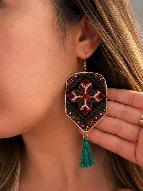 Model wearing floral embroidered shield earrings with green tassels