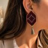 Model wearing red geometric embroidered earrings with grey-green tassels