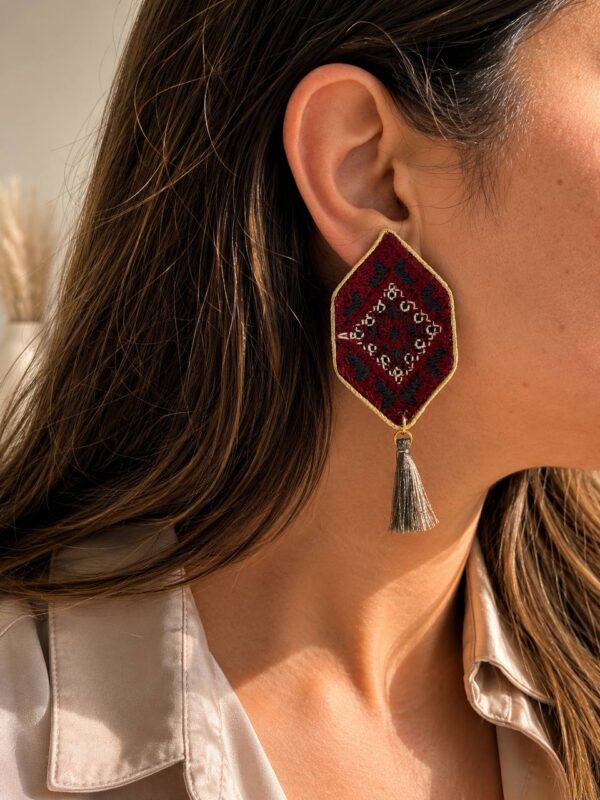 Model wearing red geometric embroidered earrings with grey-green tassels