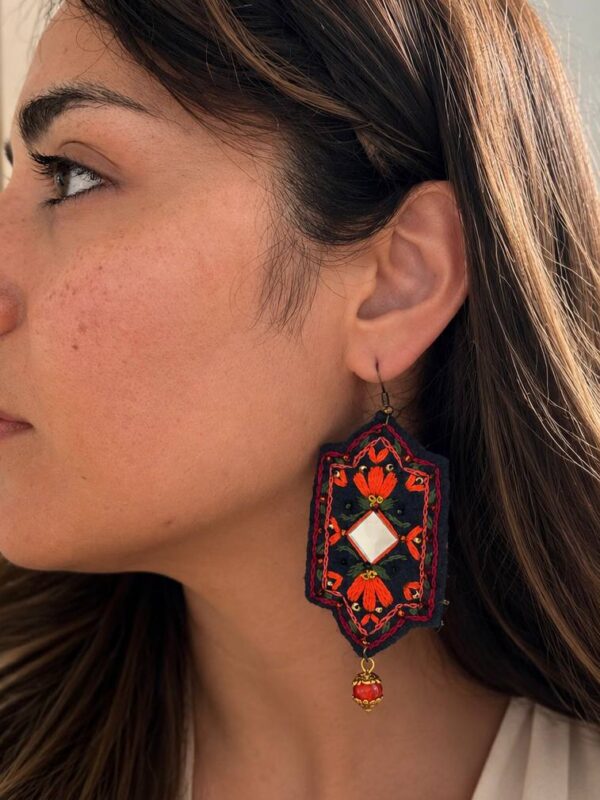 Model wearing orange floral embroidered earrings with red bead drops
