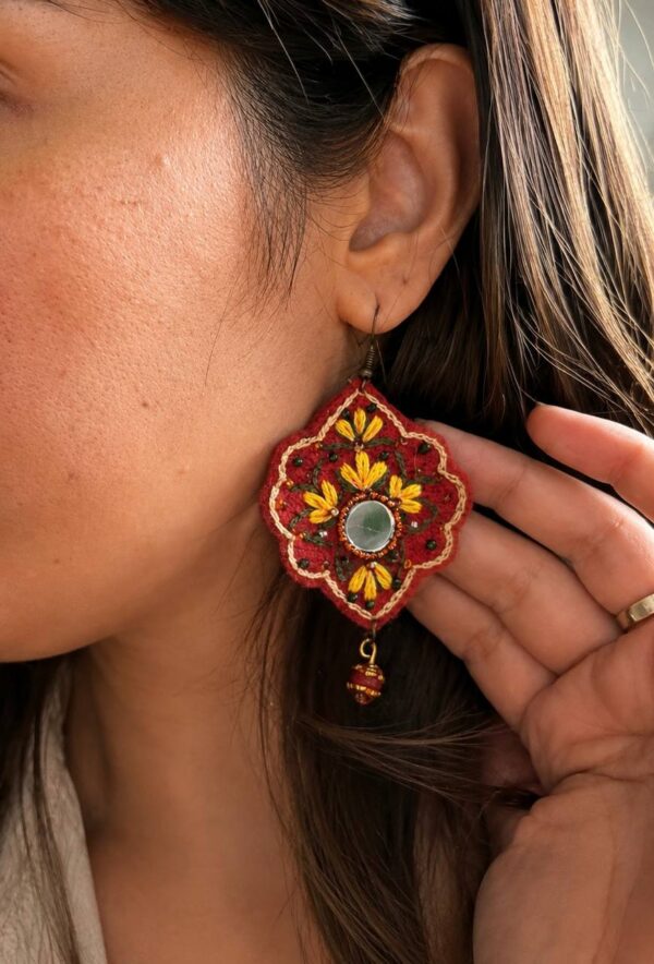 Model wearing red embroidered earrings with yellow flowers and red bead drops